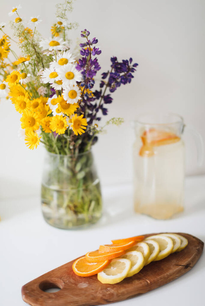 Summer concept. Bouquet of wild natural flowers. Homemade lemonade with orange and lemon. Healthy  fresh cool beverage  - Zdjęcie, obraz