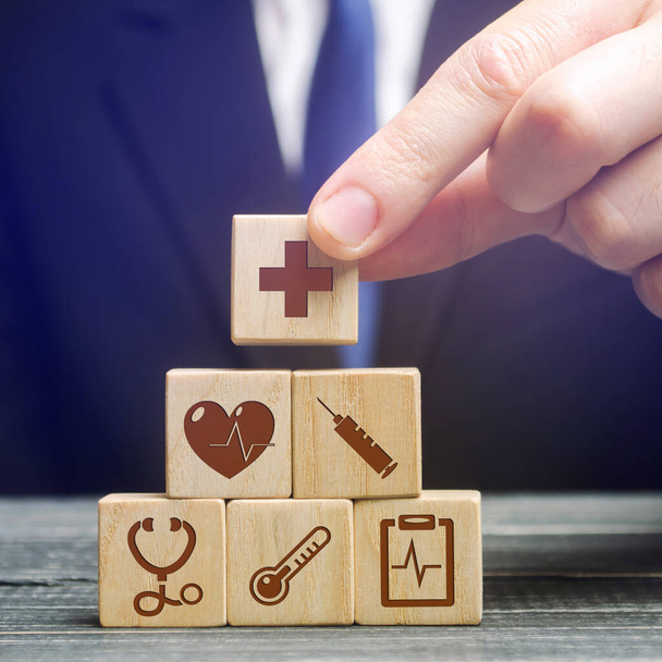 Businessman puts wooden blocks with the image of medical symbols. Healthcare and medical Insurance concept. Stethoscope, cross, thermometer and other. Medical care - Foto, immagini