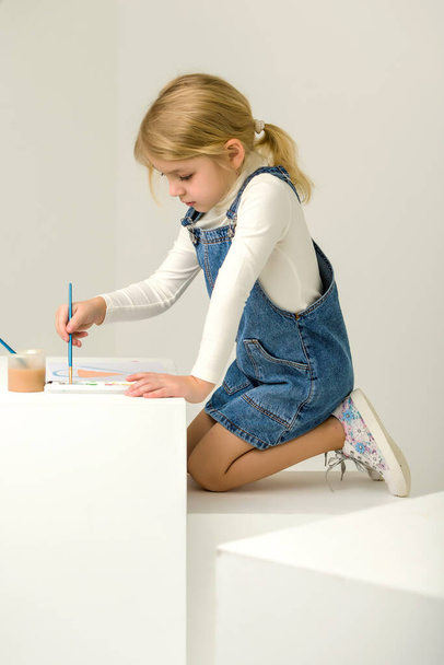 Cute Blonde Girl Sitting on Her Knees and Painting with Brush. - Фото, изображение