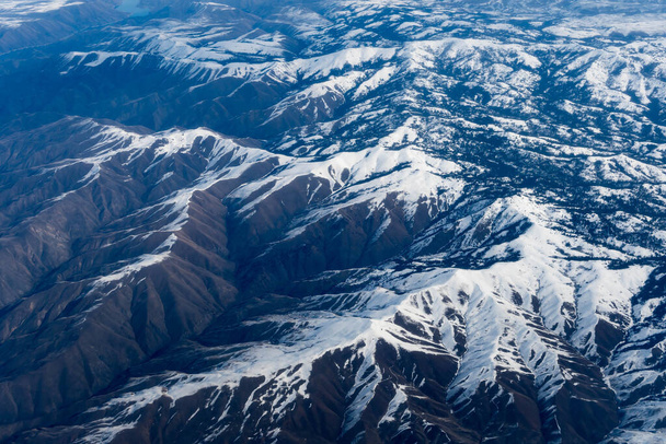 Aerial View of Idaho mountains from the sky while inside an airplane. View of brown mountains and trees covered with snow - Фото, изображение