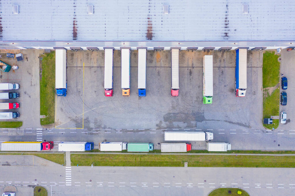 Aerial view of goods warehouse. Logistics center in industrial city zone from above. Aerial view of trucks loading at logistic center. View from drone. - Photo, Image