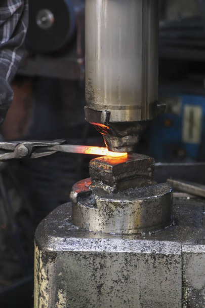 A kovács egy forró fémtárgyat dolgoz fel az üllőben egy műhelyben. A kovács munkafolyamata. Vasrúd kovácsolása az üllőn. - Fotó, kép