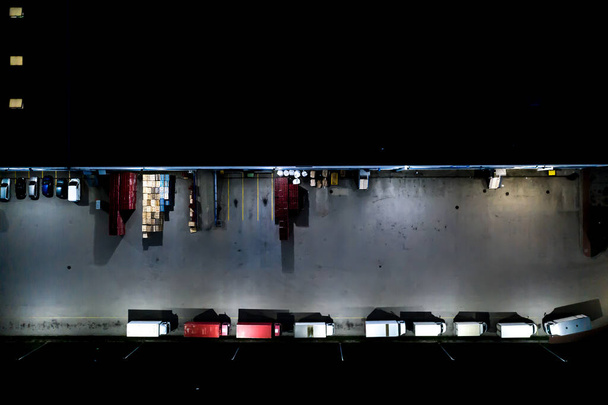 Vista aérea nocturna del almacén de mercancías. Centro logístico en zona industrial de ciudad desde arriba. Vista aérea de camiones cargando en el centro logístico. Vista desde el dron. - Foto, imagen