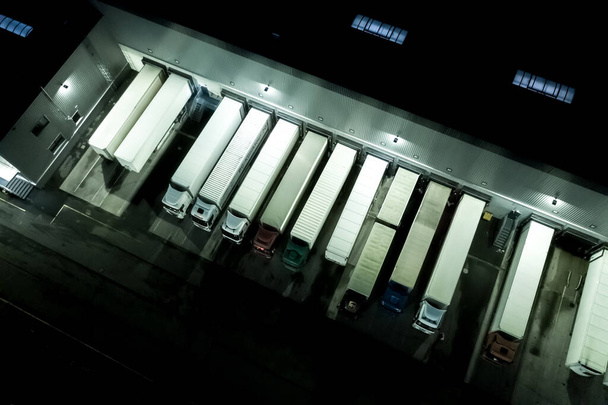 Nacht Moderne logistieke centrum, witte bestelwagen en aanhangwagens standingon helling. Luchtzicht - Foto, afbeelding