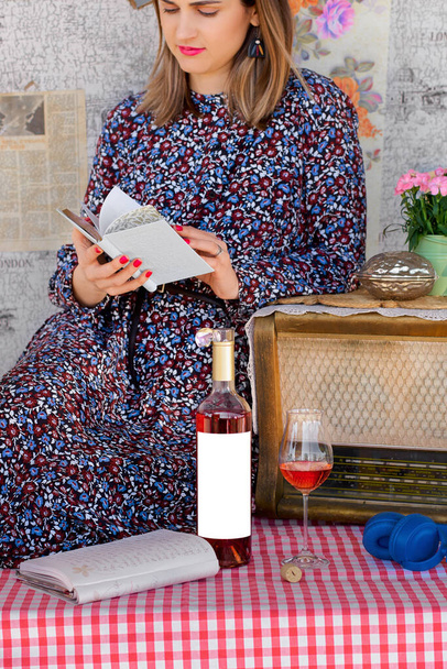 Girl with a book in hand and a glass with wine and bottle with blank etiquette for mockup. the concept of comfort and relaxation - Foto, imagen