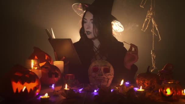 Young witch is reading the book aloud and laughs holding aroma stick - Footage, Video