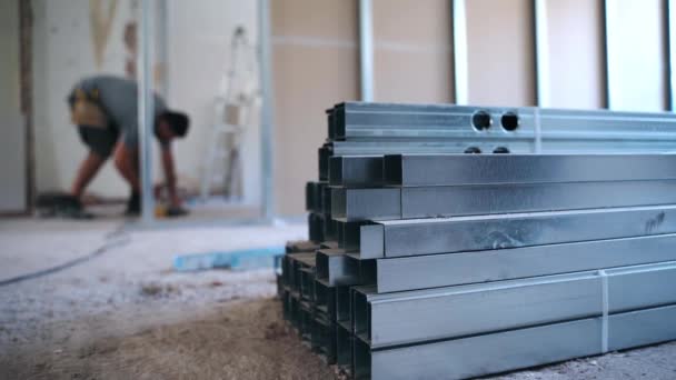 Stack of long metal construction profiles lying on blurred background of working engineer. Building worker measuring levels and distance, using electric screwdriver and drilling holes for drywalls - Footage, Video