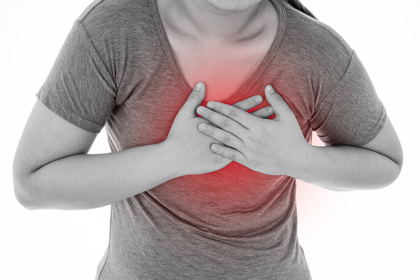 Zwart-wit shot van een vrouw die zich uitgeput voelt en lijdt aan hartpijn en letsel op een geïsoleerde witte achtergrond met rode vlek. Gezondheidszorg en medisch concept. - Foto, afbeelding