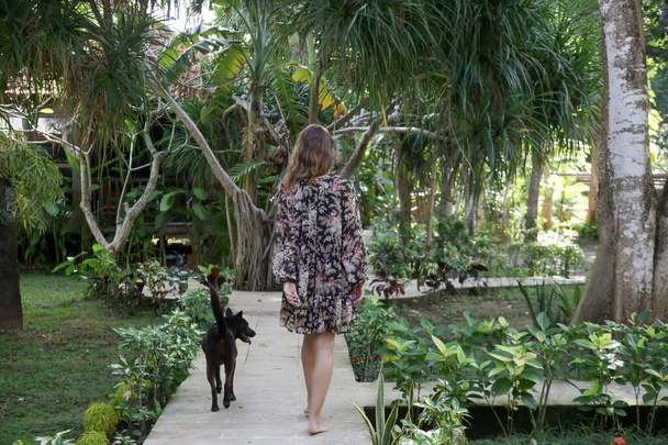 Widok z tyłu boso kobieta spacery przez tropikalny ogród z psem - Zdjęcie, obraz