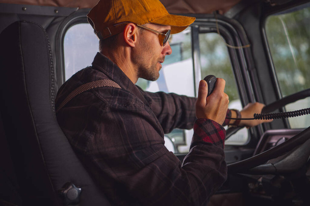 Caucasian Male Truck Driver Communicating On Two Way Radio Inside Of Vehicle Cab.  - Фото, изображение