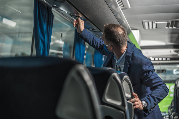 Openbare autobuschauffeur met beschermend gezichtsmasker op het controleren van de luchtventilator boven passagiersstoelen.  - Foto, afbeelding