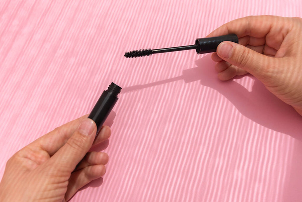 Visão superior das mãos femininas segurando rímel preto no fundo rosa pastel com sombras criativas
 - Foto, Imagem