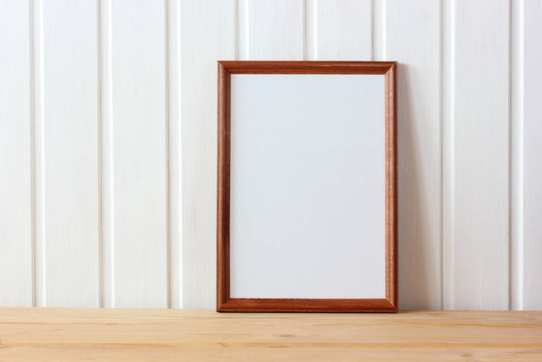 empty wooden frame on the table on the background of a white wall made of boards. mockup, scene creator. - Фото, изображение