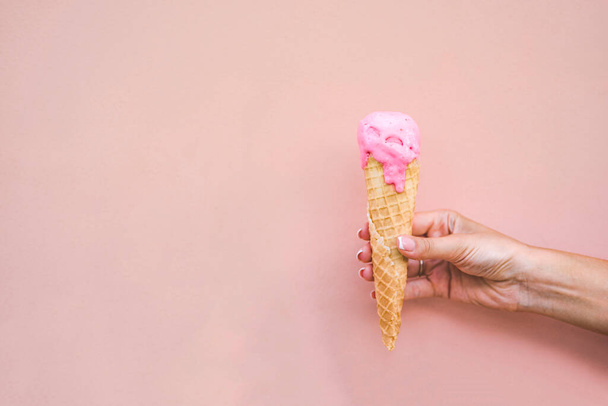 Girls hand holding melted pink strawberry ice cream cone on pink background.  - Photo, Image