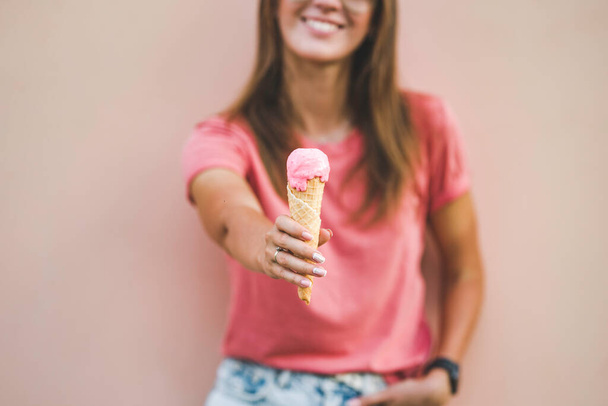 Beautiful trendy girl in pink t-shirt giving tasty ice cream on pink background. - Фото, зображення