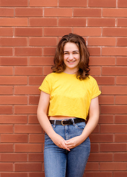 portrait of a young woman wearing yellow shirt against brick wall - Foto, Bild