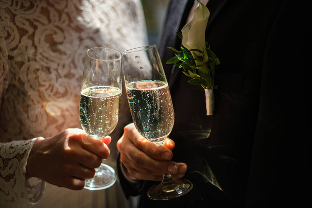 Hands of bride and groom holding champagne glasses with sparkling wine. Wedding celebration concept - Zdjęcie, obraz