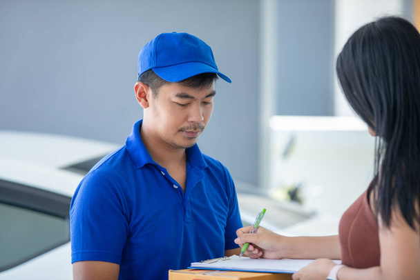 Repartidores asiáticos llevando un uniforme azul con un bluecap y manejando cajas de cartón para regalar a la clienta delante de la casa. Compras en línea y entrega Express
  - Foto, imagen