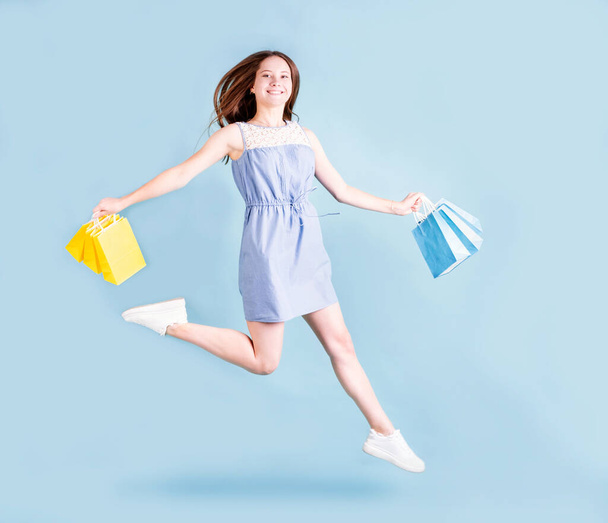 Торгова жінка. Весела молода жінка біжить і стрибає тримаючи сумки. Повна довжина ізольована на синьому фоні
. - Фото, зображення