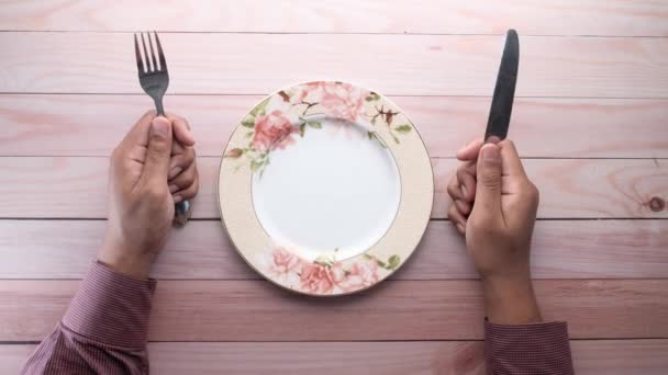 férfi villával, késsel és üres tányérral a fa asztalon. - Felvétel, videó