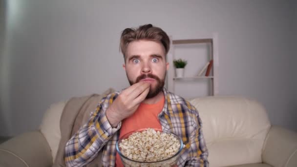Concepto de cine en casa. Impresionado y asustado hombre viendo la televisión y comiendo palomitas de maíz
 - Metraje, vídeo