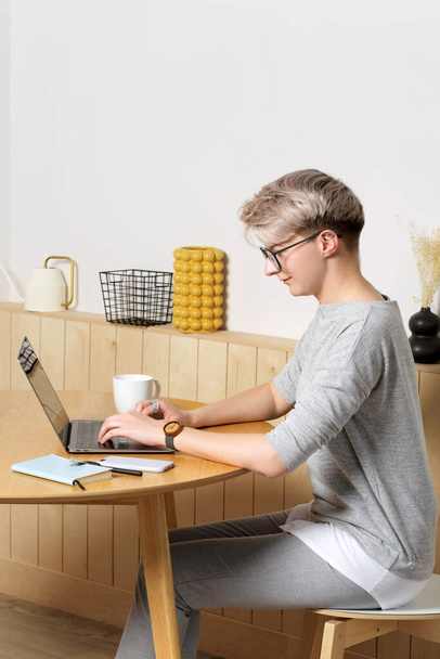 Молодая довольно хипстерская женщина тысячелетия работает с ноутбуком в интерьере кафе, боковой вид, глядя на экран и печатая
 - Фото, изображение