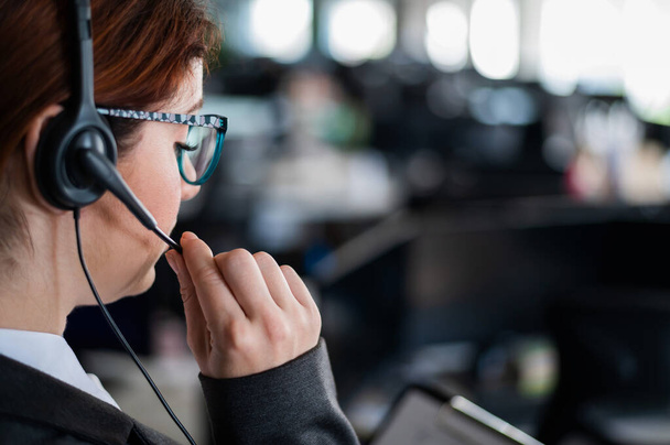 Rear view of a female helpdesk operator. An office manager with a headset answers customer calls. Unrecognizable woman in glasses works as a secretary. Employee call center. - Foto, Bild