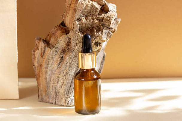 Glass cosmetic bottles with a dropper stand next to a log on a beige background with bright sunlight. The concept of natural cosmetics, natural essential oil. - Foto, Bild