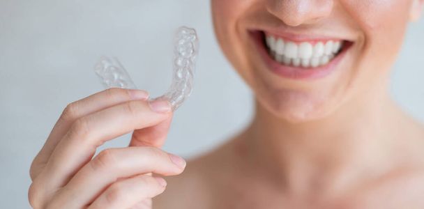 Close-up of orthodontic silicone transparent teeth aligner in female hands. Unrecognizable woman holding a removable night retainer. Bracket for teeth whitening. The perfect smile. Cropped photo. - Foto, afbeelding