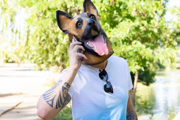 Tetovaný muž s psí maskou pomocí smartphonu, legrační blázen - Fotografie, Obrázek