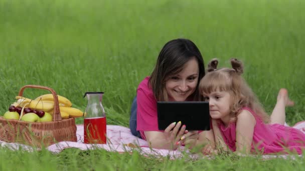 Een familie weekend picknick. Dochter kind meisje met moeder studie lessen op tablet. Afstandsonderwijs - Video
