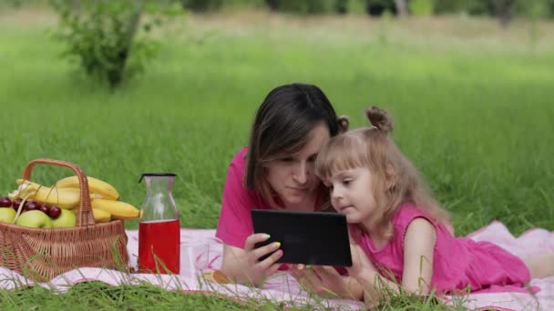 Picnic familiar de fin de semana. Hija niña con lecciones de estudio de la madre en la tableta. Educación a distancia
 - Metraje, vídeo