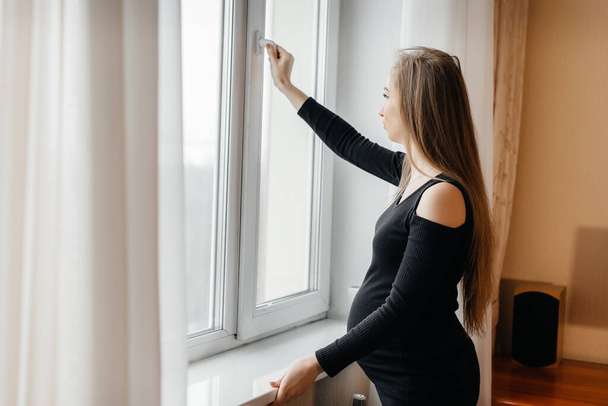 Těhotná dívka otevře okno, aby se nadýchala čerstvého vzduchu - Fotografie, Obrázek