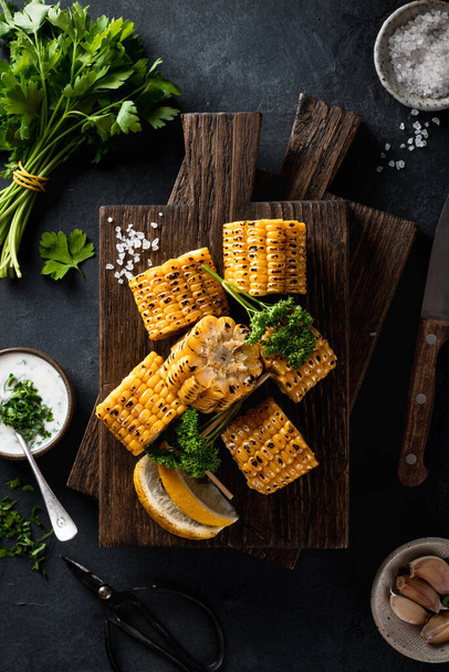 corn cobs grilled on a kitchen board on a dark stone background - Foto, afbeelding