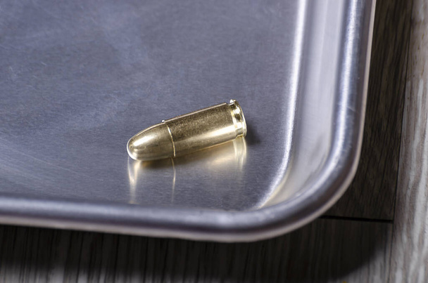 een enkele ronde munitie zit in de steriele hoek van een zilveren roestvrijstalen trey, messing glinsterend in warme verlichting - Foto, afbeelding