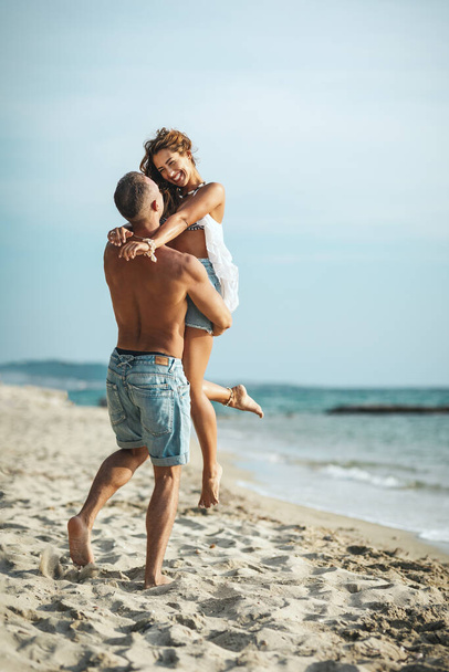loving couple having fun, hugging and playing on empty sandy sea beach - Фото, изображение