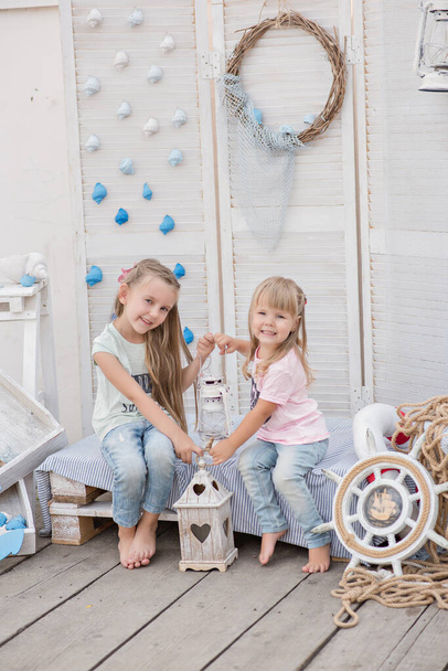 The best sisters in the world! Two little blonde girls play with shells, stars, an anchor, lanterns and marine decor, lie on the bed, laugh, hug, kiss, listen to the sounds of the sea, share secrets - Фото, зображення