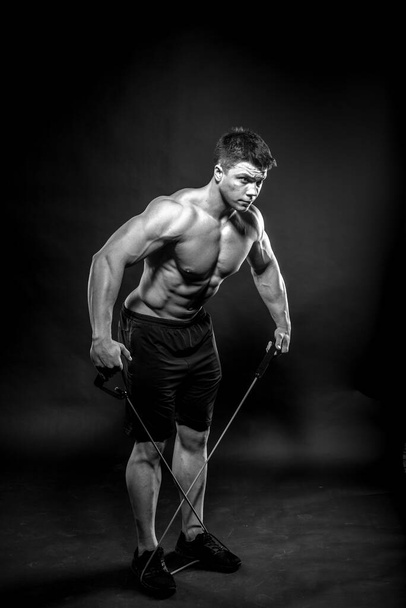 Jovem atleta sexy posando em um fundo preto no estúdio. Fitness, musculação, preto e branco - Foto, Imagem