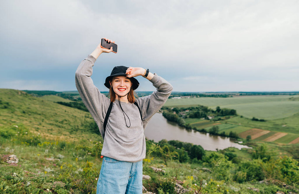 Neşeli hippi kız, elleri havada, güzel bir Ukrayna manzarasının arka planında, gölü olan dağda duruyor ve yüzünde bir gülümsemeyle kameraya bakıyor. Ukrayna 'ya seyahat. - Fotoğraf, Görsel