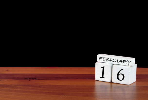 16 lutego miesiąc kalendarzowy. 16 dni w miesiącu. Refleksyjny kalendarz na drewnianej podłodze z czarnym tłem - Zdjęcie, obraz