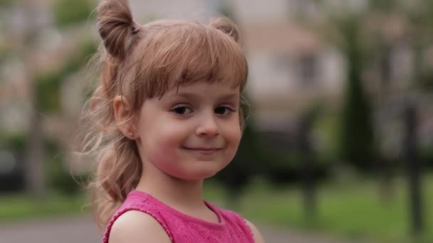 Little child girl against the blurred city street background. Cheerful, positive emotions, smile - Footage, Video