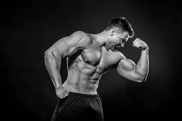 Sexy young athlete posing on a black background in the Studio. Fitness, bodybuilding, black and white - Photo, image