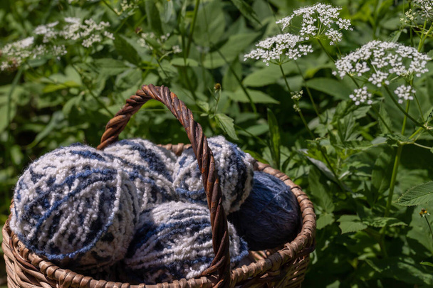 White-blue fluffy woolen balls in a basket on a natural background of white summer flowers. Horizontal poster with copy space. Yarn for knitting. Items of female needlework. - Photo, Image