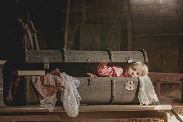 Little child, boy, hiding in old vintage suitcase in the attic, scared not to be found - Foto, afbeelding