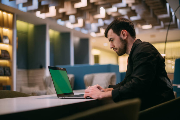 Ein Mann arbeitet an einem Laptop in einem Büro oder Coworking. Jungunternehmer in stilvoller Kleidung mit Computer an einem modernen Arbeitsplatz. - Foto, Bild