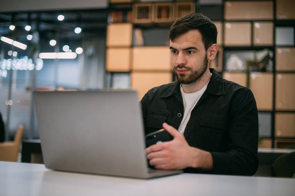 Человек работает на ноутбуке в офисе или коллеге. Молодой бизнесмен в стильной одежде с компьютером на современном рабочем месте. - Фото, изображение
