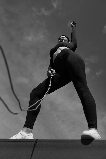 Bottom view black and white photo of a girl trainer holding a rope in hand against the sky in a park on the street - Photo, image