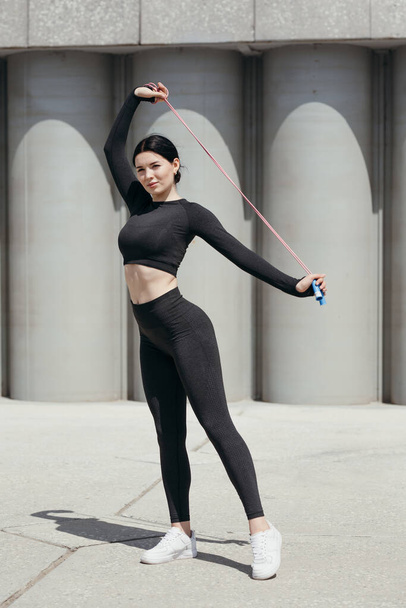 Belle fille asiatique en forme faisant des exercices d'échauffement sur les muscles trapèzes du dos avec une corde à sauter sur la promenade dans le parc - Photo, image