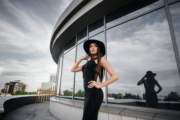 Stylish young and sexy girl posing in front of a business center in black. Fashion and style - Фото, зображення