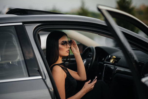 Stylish young girl sitting in a business class car in a black dress. Business fashion and style - Fotografie, Obrázek